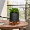 3D-Druck Pflanztopf TALO in dunkler Fuzzy Skin Optik mit braunem Ständer auf einem Holztisch dekoriert.