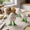 Ein lustiger Dino Eierbecher aus dem 3D-Drucker, in dem ein weisses Ei steckt, dekoriert auf einem morgendlichen Frühstückstisch.
