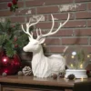 Eine weisse, abstrakte Hirsch Skulptur aus dem 3D-Drucker, die elegant auf einem dunklen Holztisch neben weihnachtlicher Deko steht.