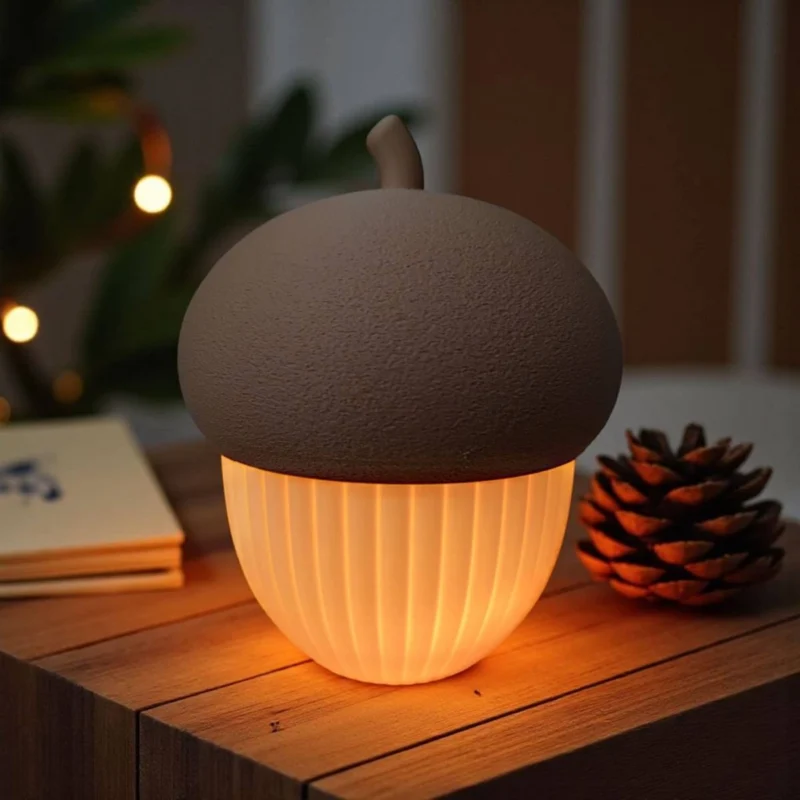 Ein beleuchteter Eichel Teelichthalter aus dem 3D-Drucker, der an einem Herbstabend gemütliches LED-Licht auf einem Holztisch verströmt.