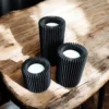 Ein schwarzes geripptes Teelichthalter Set aus dem 3D-Drucker, bestehend aus drei unterschiedlich hohen Haltern, stilvoll beleuchtet mit LED-Teelichtern auf einem rustikalen Holztisch.