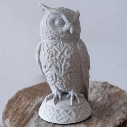 Eine hellgraue Keltische Eulen Skulptur aus dem 3D-Drucker mit detailreichen Ornamenten, die auf einem rustikalen Holztisch dekoriert ist.