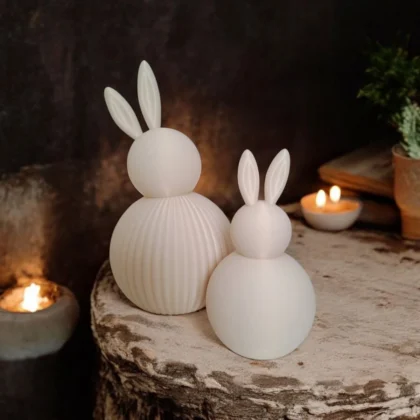 in weisses, modernes Osterhasen Set aus dem 3D-Drucker, das harmonisch im warmen Kerzenschein auf einem rustikalen Holzstamm dekoriert ist.