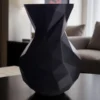 Eine schwarze minimalistische Low Poly Vase aus dem 3D-Drucker, die stilvoll in einem modernen Wohnambiente auf einem Tisch dekoriert ist.