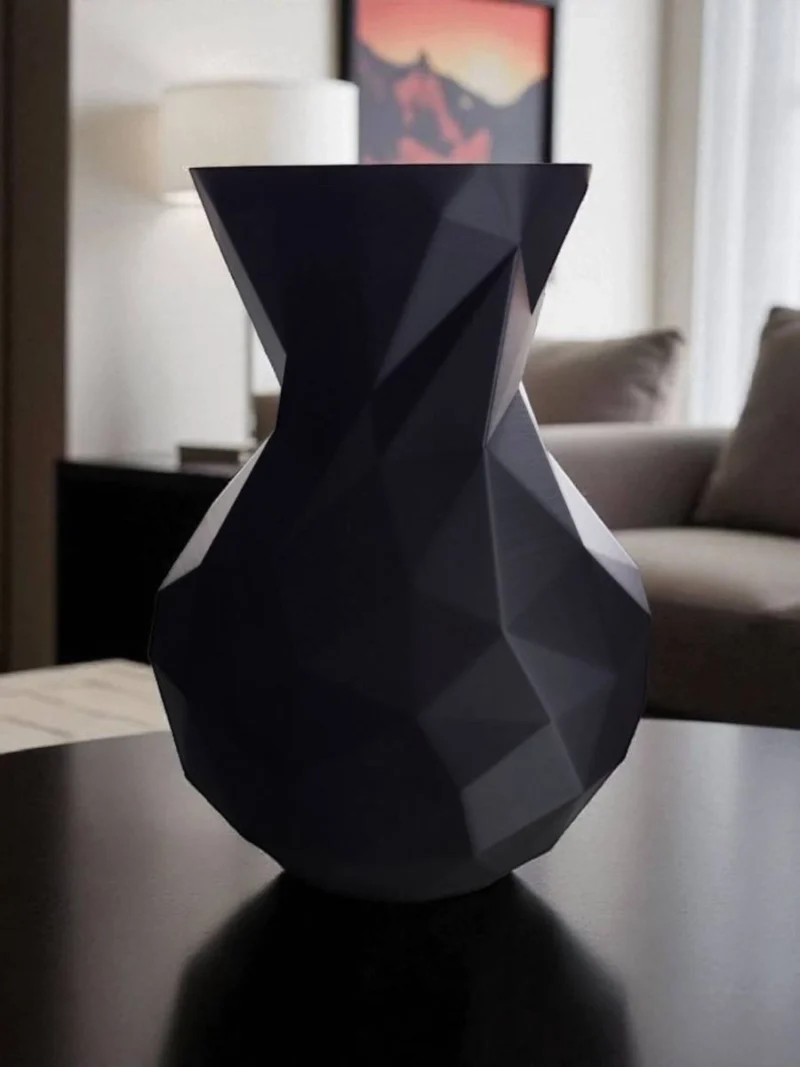 Eine schwarze minimalistische Low Poly Vase aus dem 3D-Drucker, die stilvoll in einem modernen Wohnambiente auf einem Tisch dekoriert ist.