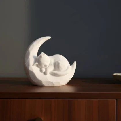 Eine weisse Katze auf Mond Skulptur aus dem 3D-Drucker, die friedlich schlafend auf einem Regal aus dunklem Holz dekoriert ist.