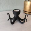 Ein schwarzer Oktopus Teelichthalter aus dem 3D-Drucker, der mit einem leuchtenden LED-Teelicht stilvoll auf einem hellen Tisch dekoriert ist.