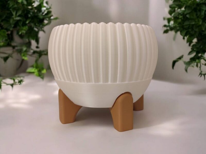 Weisser Mid-Century Blumentopf namens Luma mit dicken Rillen, der auf einem hellbraunen vierbeinigen Gestell in einem modernen Wohnzimmer steht.