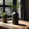Eine dunkelgrüne minimalistische Feldflaschen Vase aus dem 3D-Drucker, die stilvoll mit grünen Zweigen auf einem Holztisch vor einem Fenster dekoriert ist.