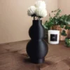 ine schwarze geschwungene Design Vase aus dem 3D-Drucker mit edler Fuzzy-Skin-Struktur, dekoriert mit weissen Blumen auf einem dunklen Holztisch.