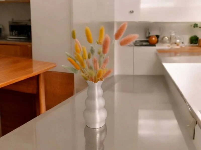 Eine weisse Tulpen Design Vase aus dem 3D-Drucker mit rauer Fuzzy-Skin-Oberfläche, die mit bunten Trockenblumen auf einem Holztisch dekoriert ist.