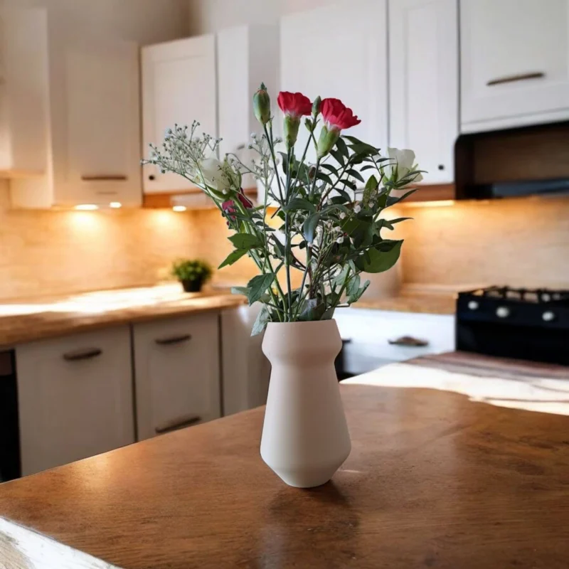 Eine cremefarbene moderne Kegel Vase aus dem 3D-Drucker, die stilvoll mit frischen Blumen auf einer Holzanrichte in der Küche dekoriert ist.