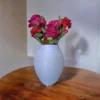 Eine weisse moderne Rillen Vase aus dem 3D-Drucker, die stilvoll mit frischen roten Rosen auf einem dunklen Tisch dekoriert ist.