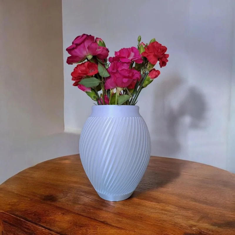 Eine weisse moderne Rillen Vase aus dem 3D-Drucker, die stilvoll mit frischen roten Rosen auf einem dunklen Tisch dekoriert ist.