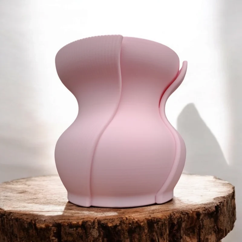 Eine rosa skulpturale Design Vase Aera aus dem 3D-Drucker mit doppelwandiger Struktur, die elegant auf einer rustikalen Holzscheibe präsentiert wird.