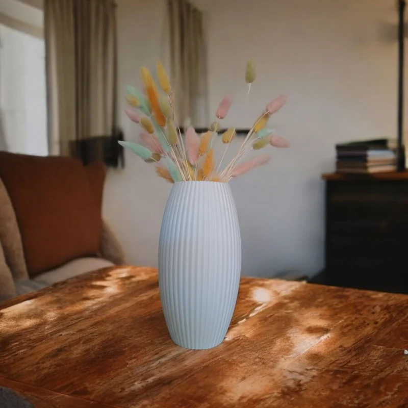 Eine weisse grosse gerippte Vase aus dem 3D-Drucker, die als elegantes Designobjekt auf einem rustikalen Holztisch steht.