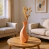 Eine sanft pfirsichfarbene minimalistische Vase Aura aus dem 3D-Drucker, die stilvoll mit getrocknetem Pampasgras auf einem hellen Holztisch steht.