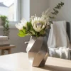 Eine weisse gedrehte Design Vase aus dem 3D-Drucker mit feinem Twist, dekoriert mit weissen Blumen auf einem hellen Holztisch.